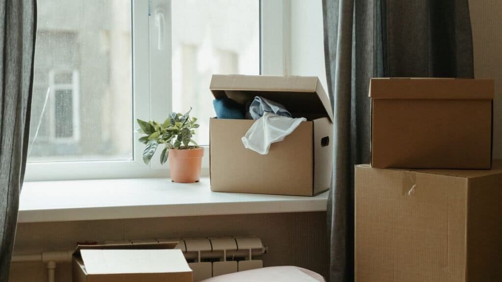 Cardboard moving boxes stacked in a sunlit, otherwise empty first apartment
