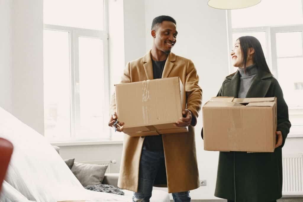first apartment move-in costs - couple carrying moving boxes into a new apartment