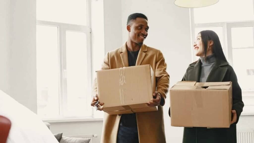 first apartment move-in costs - couple carrying moving boxes into a new apartment