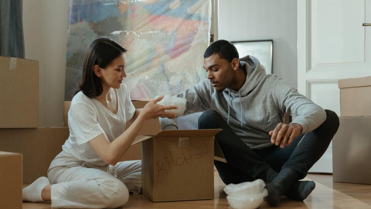 couple unpacking cardboard boxes on the floor of a first apartment