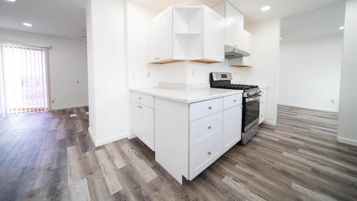 empty apartment kitchen with white cabinets and daylight from a side window