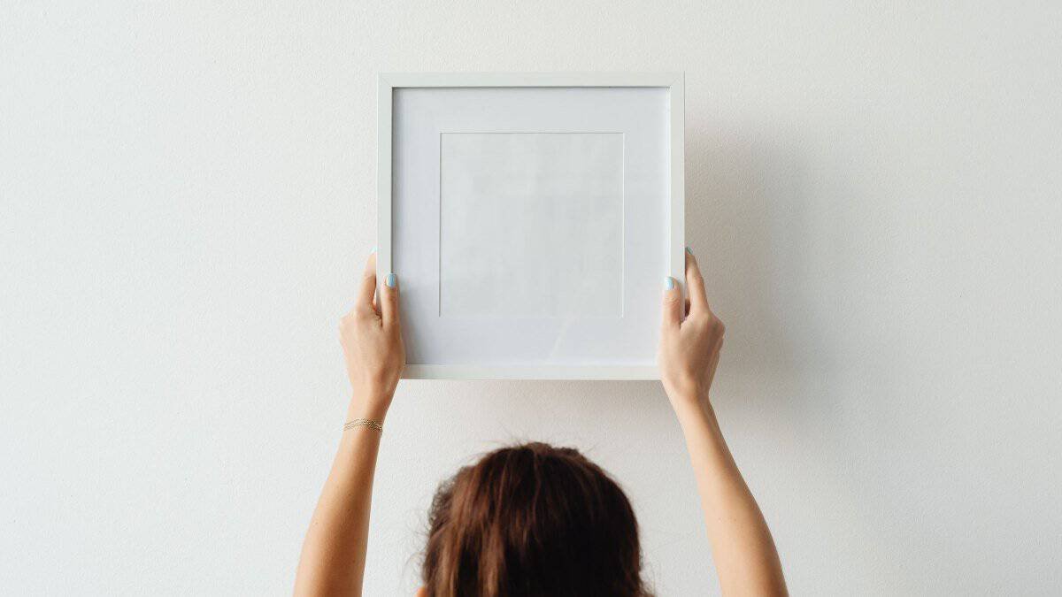 person holding a picture frame flat against a plain rental wall
