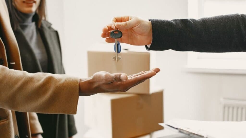 landlord handing apartment keys to a new renter with moving boxes in the background